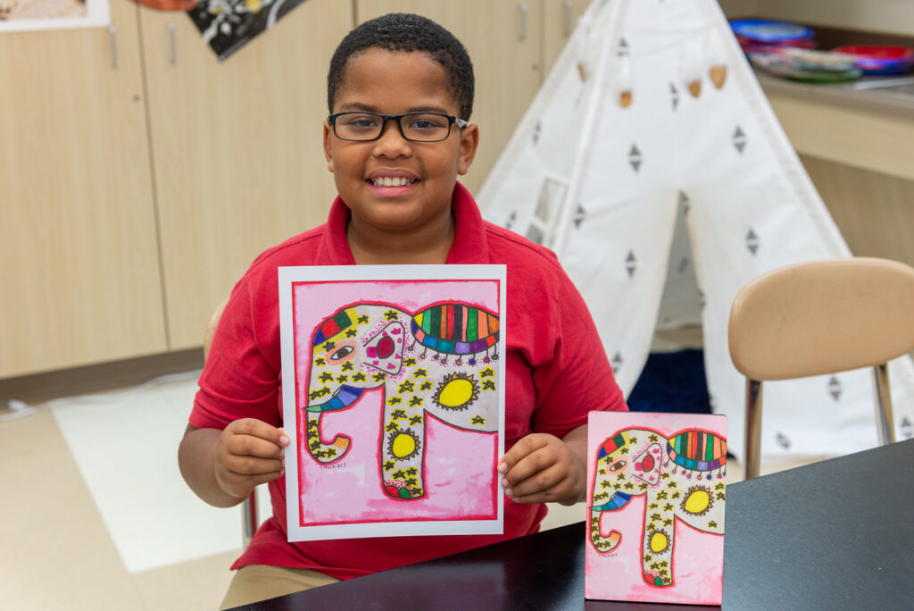 Hold an Art Fundraiser for Schools with Art to Remember image shows boy holding up artwork featuring elephant