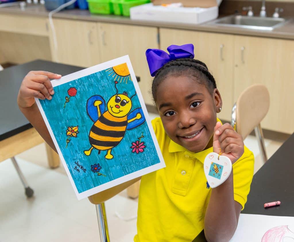 Host an Art Fundraiser for Schools by working with Art to Remember image shows girl holding up artwork