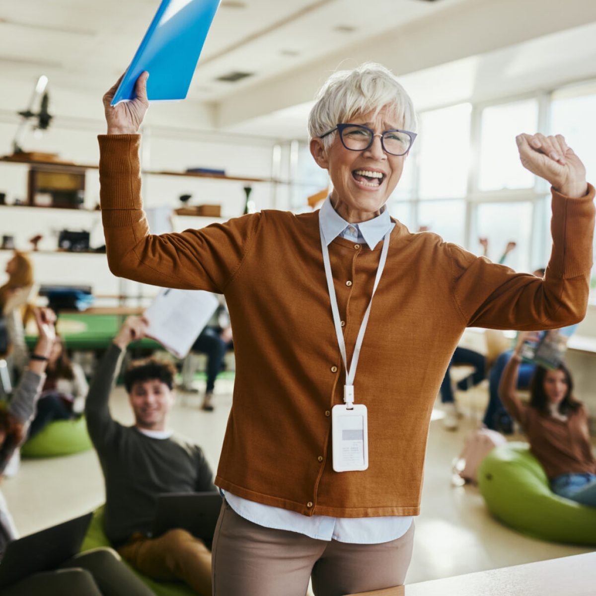 Cheerful senior professor and her students in the background celebrating the end of school year in campus.